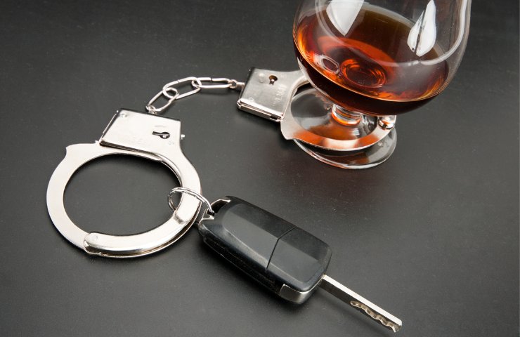Un bicchiere di whisky con manette e chiavi di un'auto