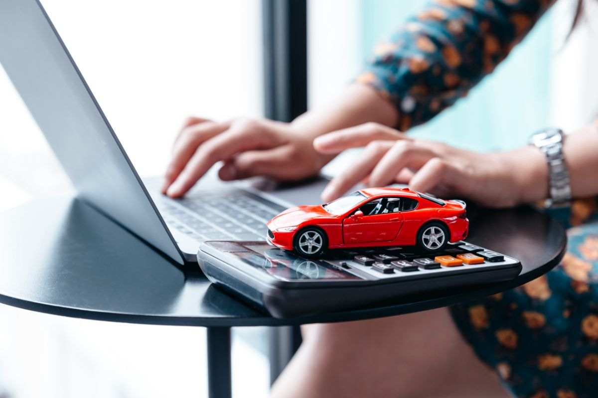 persona al pc, modellino auto e calcolatrice